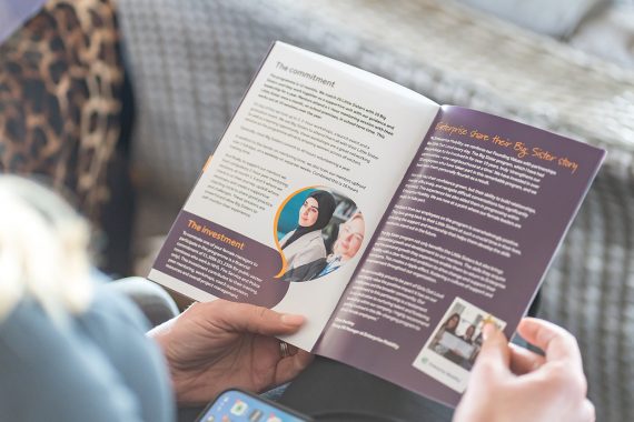Woman looking at an open leaflet all about becoming a Big Sister for Girls out loud.